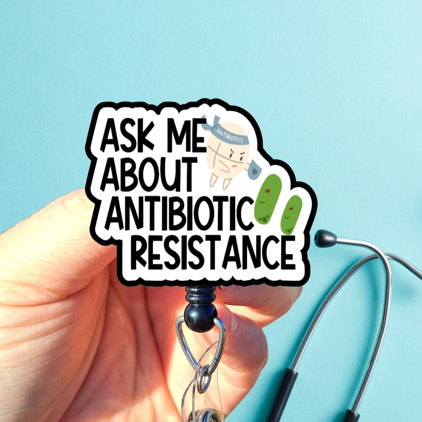 Hand holding a badge reel with 'Ask Me About Antibiotic Resistance' text against a blue background