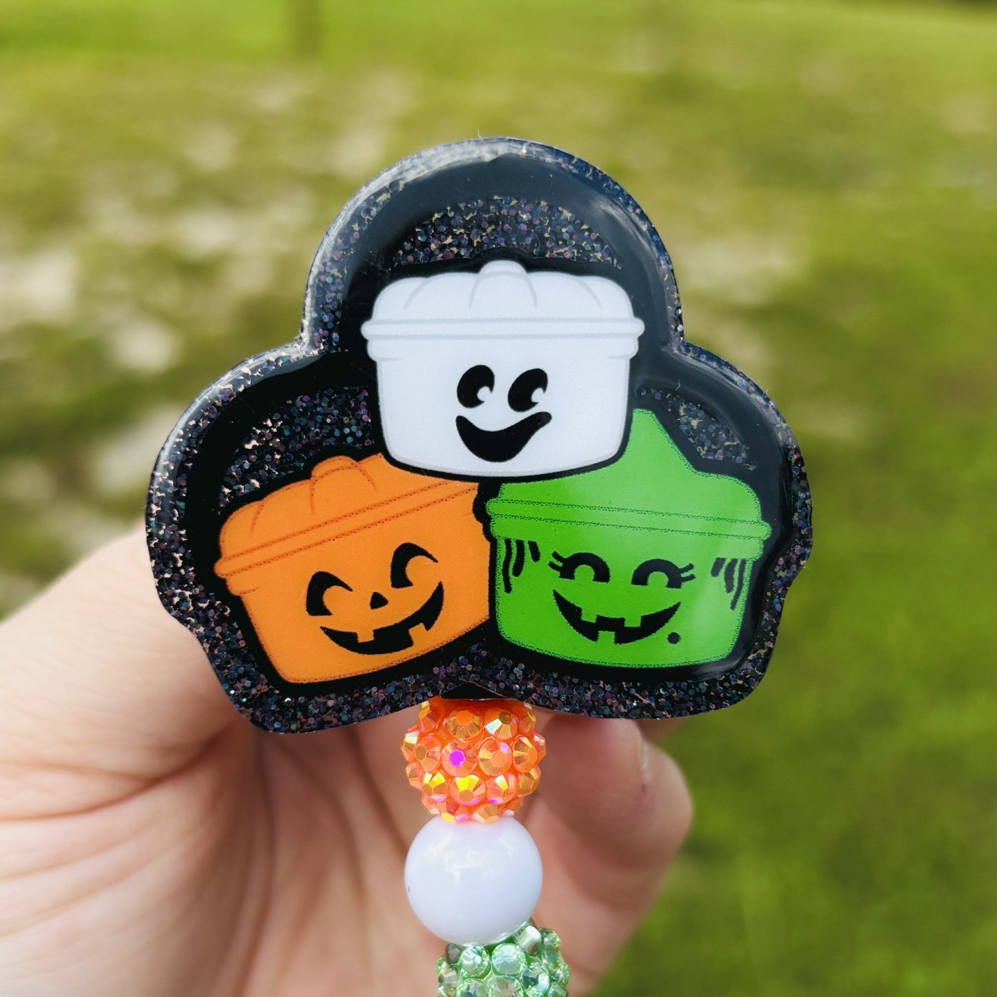 Halloween-themed badge holder with pumpkins, ghost, and witch hat design on a blurred green background.