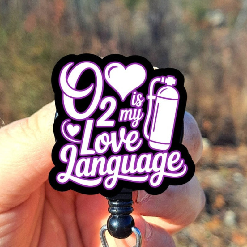 Hand holding a badge reel with 'O2 is my love language' text against a natural background