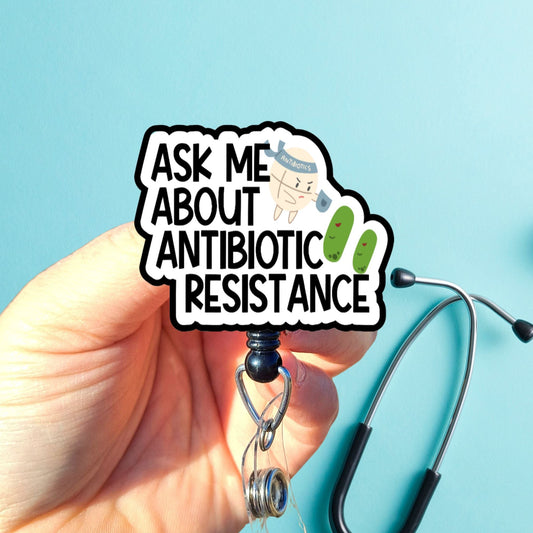 Hand holding a badge reel with 'Ask Me About Antibiotic Resistance' text against a blue background