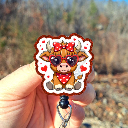 Hand holding a cartoon cow badge holder with a red bow against a natural background