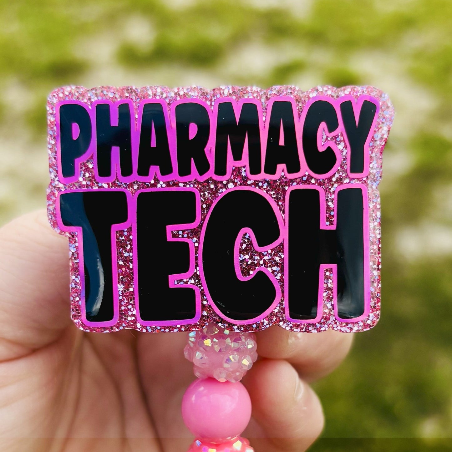 Pink and black 'PHARMACY TECH' badge holder held by a hand with a blurred green background