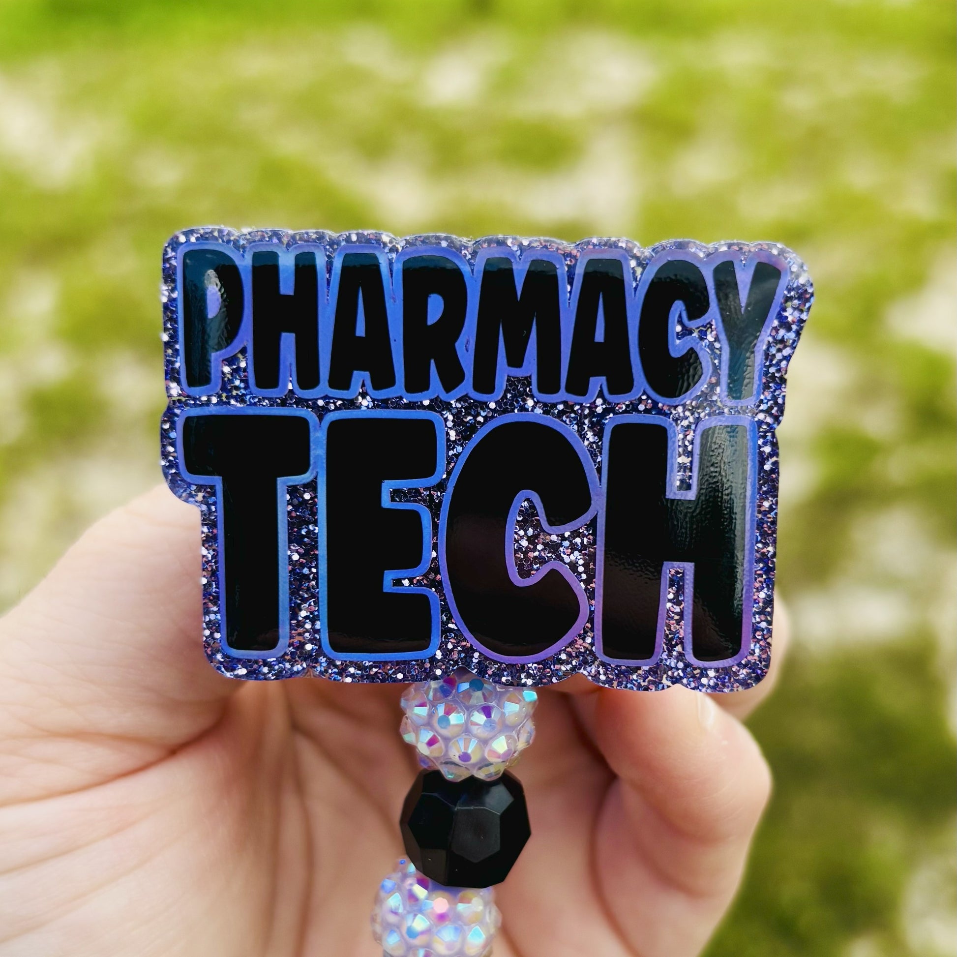 Decorative badge holder with 'PHARMACY TECH' text held by a hand against a blurred green background